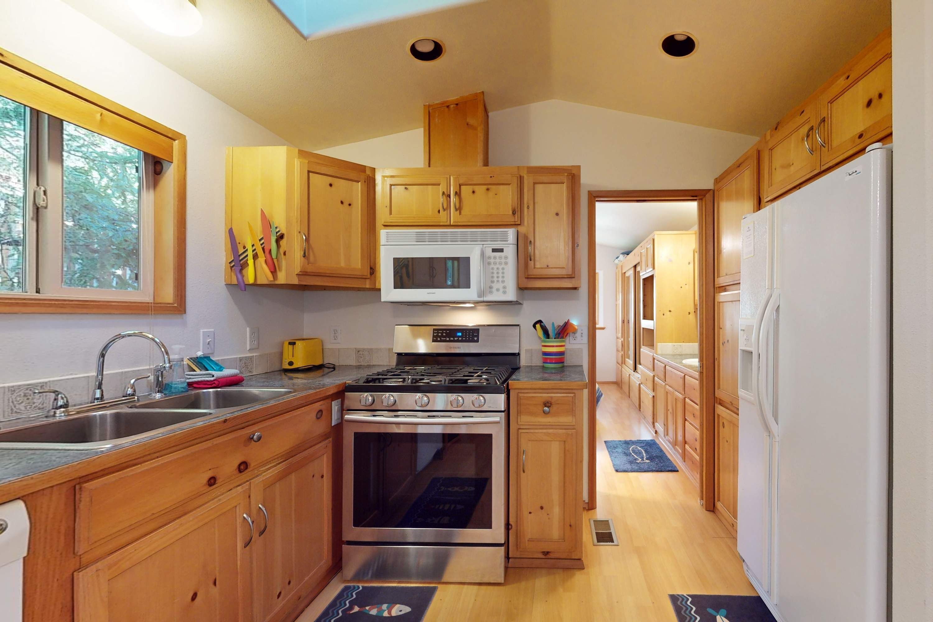 A kitchen with wooden cabinets, a microwave, stove, sink, and a refrigerator.