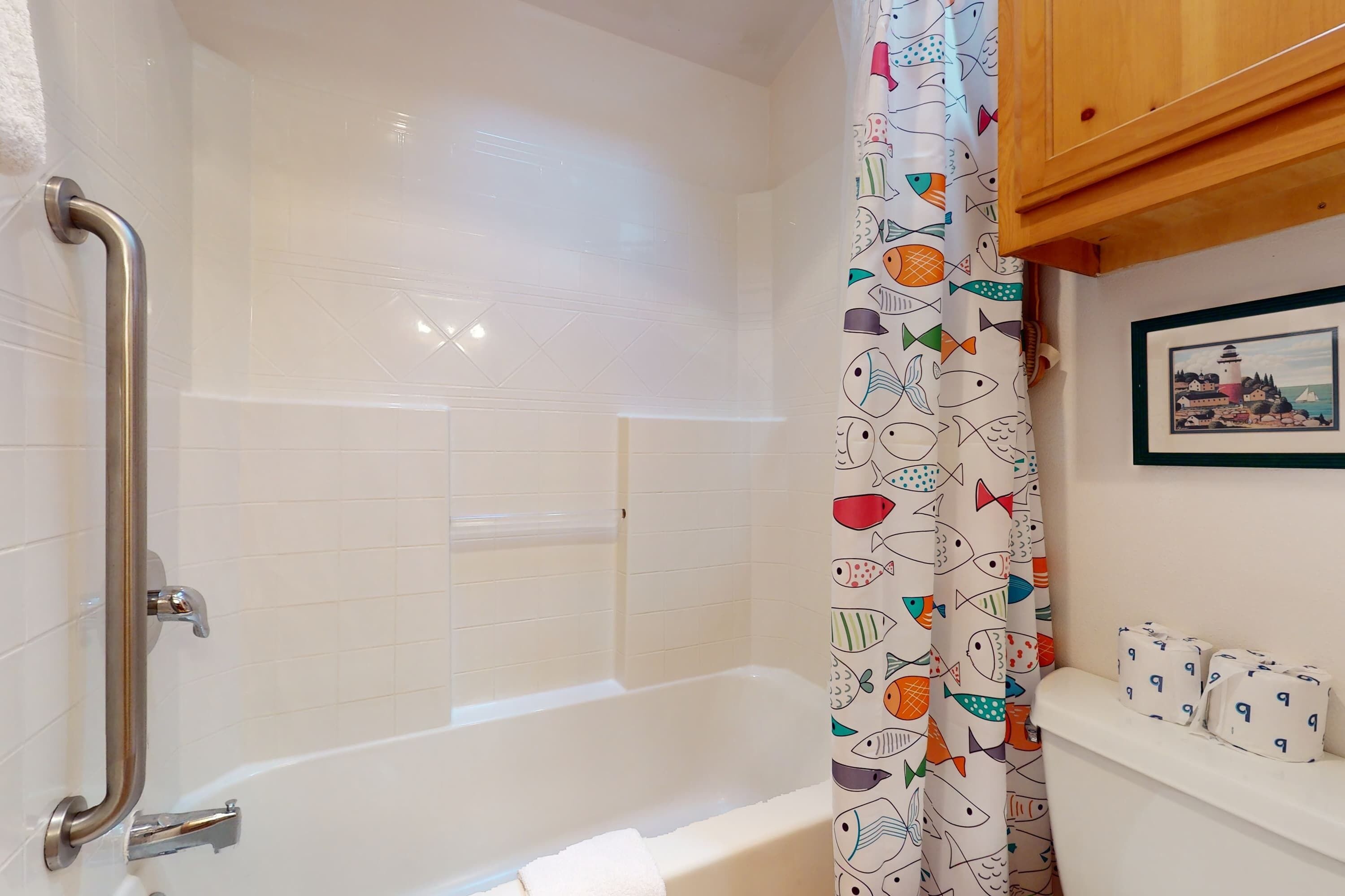 A bathroom with a white bathtub, a shower with a metal grab bar, and a fish-patterned shower curtain.