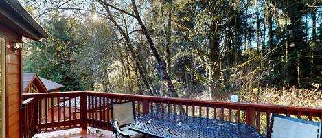 A wooden deck with a metal table and chairs, surrounded by trees.