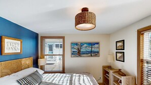 Een slaapkamer met een bed, een raam met jaloezieën, een schilderij en een plafondlamp.