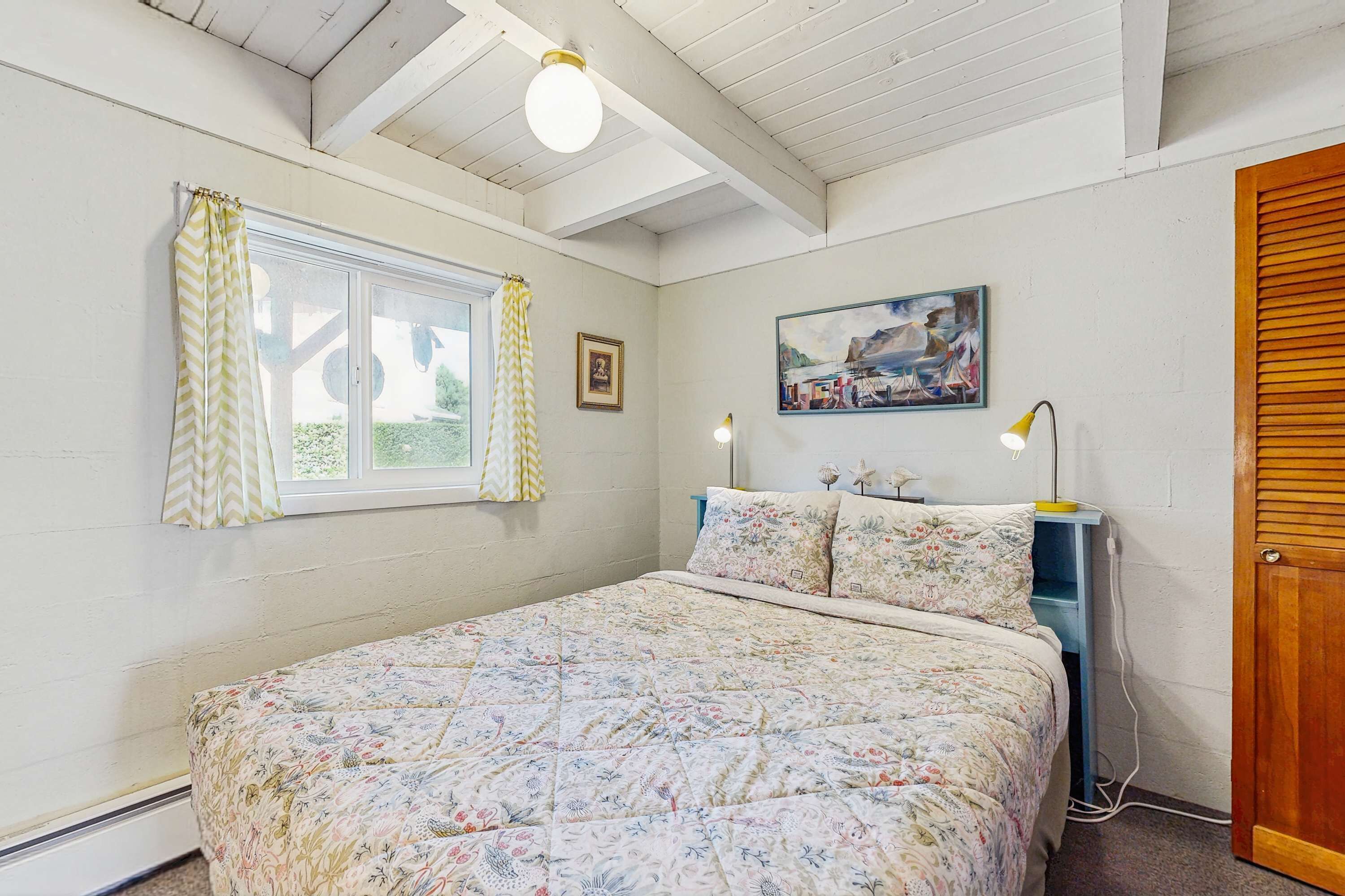 Un dormitorio con cama, ventana con cortinas, un cuadro en la pared y una lámpara de noche.
