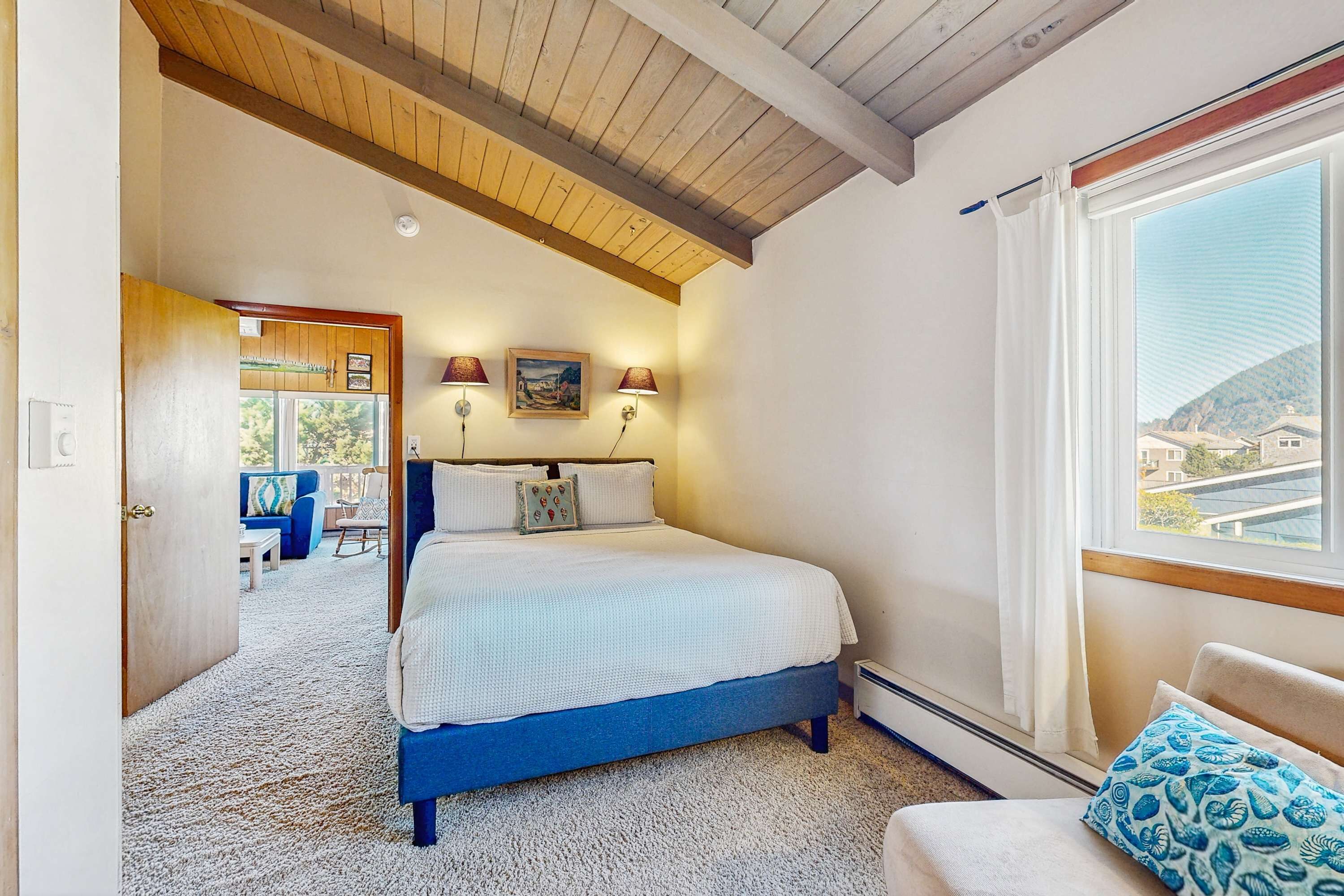 Ein Schlafzimmer mit Bett, Fenster, Tür und Blick ins Freie.