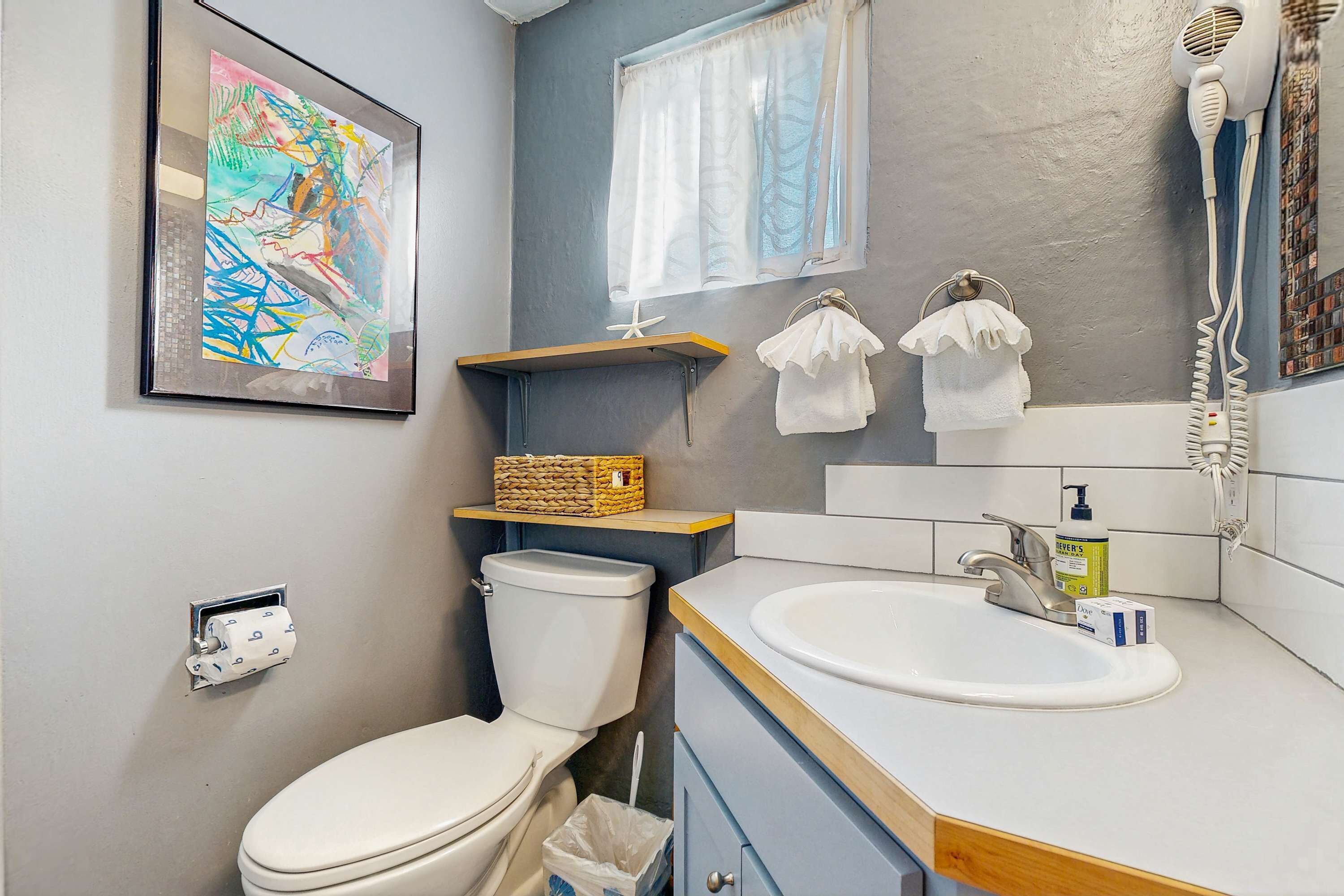 Une salle de bain équipée de toilettes, d’un lavabo, d’un porte-serviettes et d’un tableau abstrait encadré.