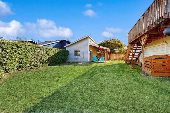 A residential backyard with a house, a wooden deck, and a well-maintained lawn. - Dog-friendly home with electric fireplace, enclosed yard, deck, beach access (Manzanita)