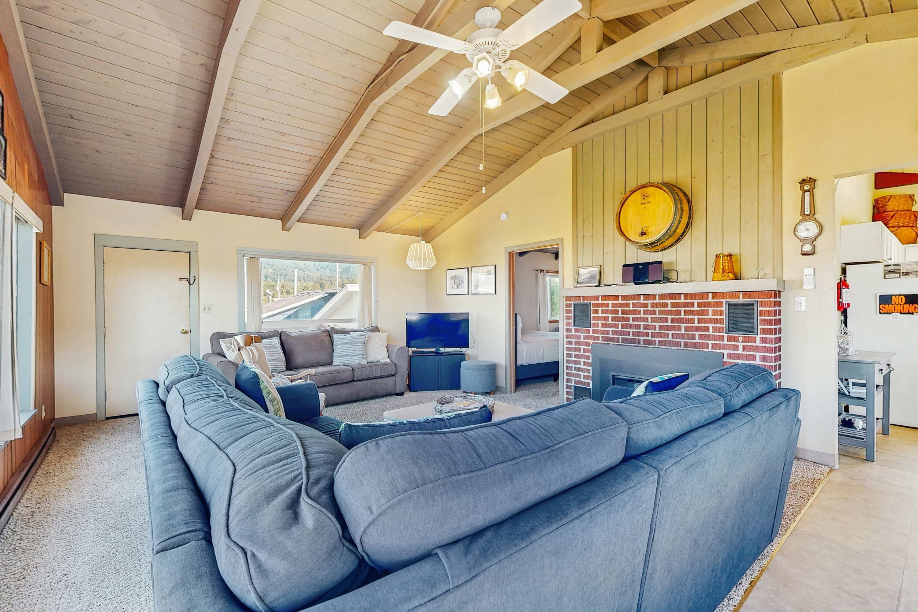 Ein geräumiges Wohnzimmer mit einem großen, grauen Ecksofa, einem Kamin und einem Deckenventilator.