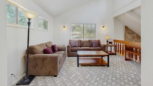A spacious living room with two sofas, a coffee table, a lamp, and a staircase with a stone wall. - Family-Friendly Home with SHARC Passes & Private Hot Tub (Sunriver)