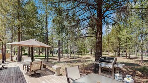 An outdoor deck with a table, chairs, a grill, and a large umbrella. - Family-Friendly Home with SHARC Passes & Private Hot Tub (Sunriver)
