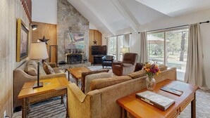 A spacious living area with a stone fireplace, comfortable seating, and a large window offering a view. - Family-Friendly Home with SHARC Passes & Private Hot Tub (Sunriver)