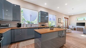 A modern kitchen with grey cabinets, a wooden countertop, and a central island. - Newly Built, Dog-Friendly, Colorful Creekside Home - One Mile to the Ocean (Gold Beach)
