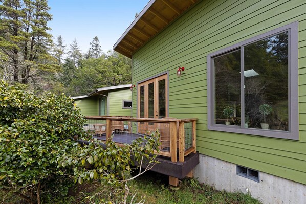 A green building with a wooden deck, large windows, and a door.