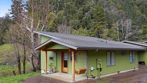 A green house with a porch, a swing, and a small front yard. - Newly Built, Dog-Friendly, Colorful Creekside Home - One Mile to the Ocean (Gold Beach)
