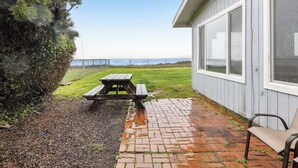 Eine Terrasse mit Picknicktisch und Stuhl, eine Rasenfläche und Blick auf den Ozean.
