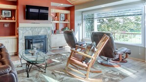 A living room with a fireplace, a television, and a large window with a view of trees.