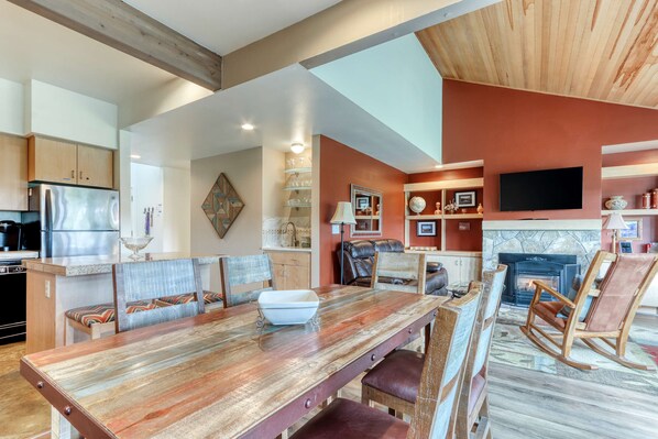 A spacious living area with a wooden dining table, seating, a fireplace, and a television mounted on the wall.