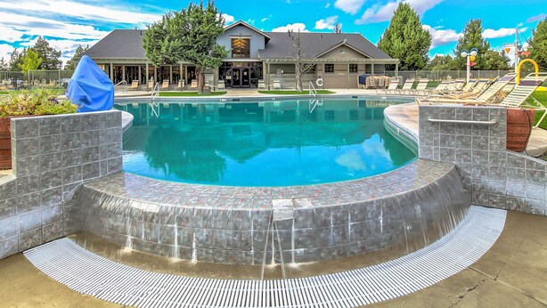 A swimming pool with a tiled deck, a covered area, and a building in the background.