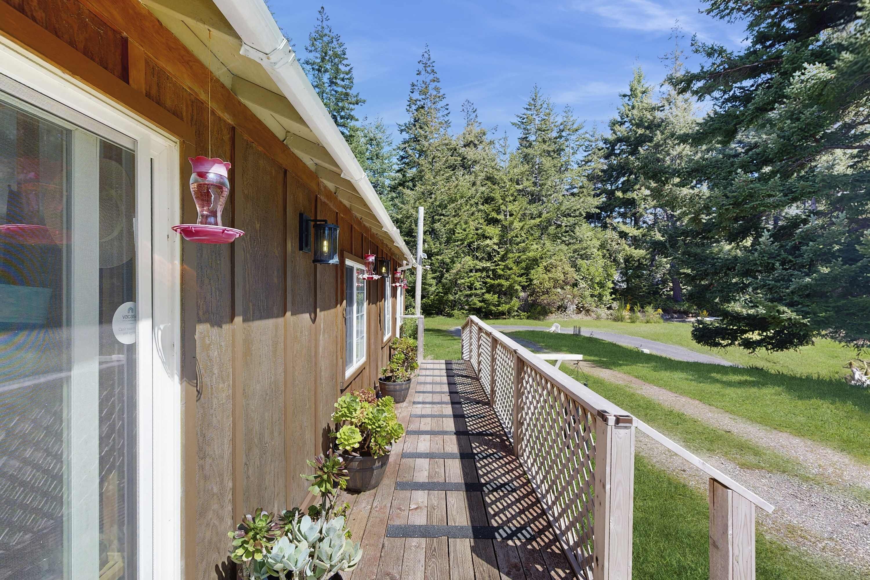 A wooden deck with potted plants, a railing, and a view of a forest.