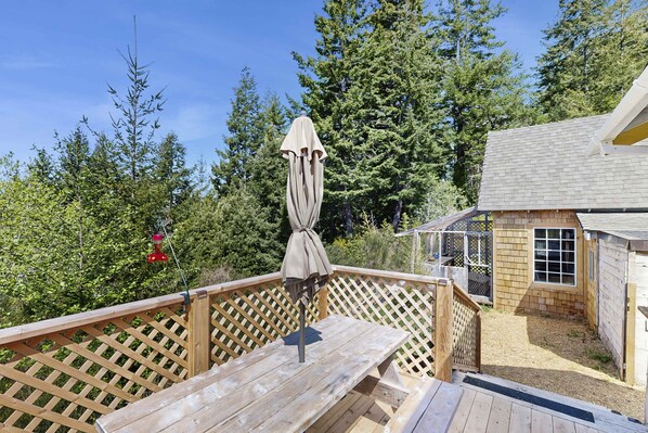 A wooden deck with a picnic table and an umbrella, surrounded by a wooden fence and trees.