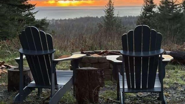 Due poltrone Adirondack rivolte verso un tramonto su un corpo d'acqua, con una foresta sullo sfondo.