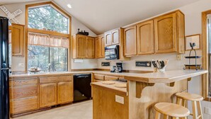 A kitchen with wooden cabinets, a built-in dishwasher, a large window, and a bar area with stools. - Inviting home with deck, gas grill, hot tub, pools, and SHARC passes (Sunriver)