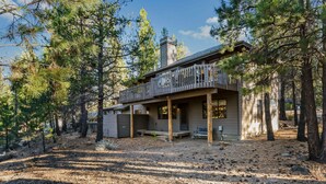 A two-story cabin with a deck, surrounded by pine trees. - Inviting home with deck, gas grill, hot tub, pools, and SHARC passes (Sunriver)