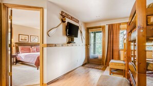 A room with a bed, a television mounted on the wall, a wooden bench, and a sign that reads 'WELCOME CAMPERS'. - Inviting home with deck, gas grill, hot tub, pools, and SHARC passes (Sunriver)