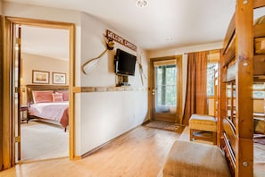 Ein Zimmer mit einem Bett, einem an der Wand befestigten Fernseher, einer hölzernen Bank und einem Schild mit der Aufschrift 'WELCOME CAMPERS'.