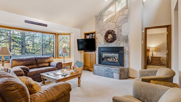 A living room with a stone fireplace, a television, and a bookshelf. - Inviting home with deck, gas grill, hot tub, pools, and SHARC passes (Sunriver)