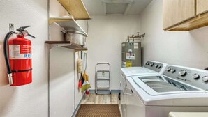 Ein Waschraum mit Feuerlöscher, Waschmaschine, Wäscheständer und Warmwasserbereiter.
