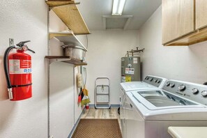 A laundry room with a fire extinguisher, a washing machine, a drying rack, and a water heater.