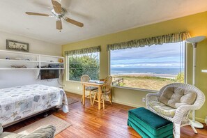 A bedroom with a bed, a desk, chairs, a window with a view of the beach, and a ceiling fan. - Dog-friendly oceanfront home on a bluff with spectacular views (Bandon)