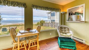 Una habitación con vistas a la playa, una mesa de comedor con sillas, un sillón acolchado y un pequeño reposapiés.