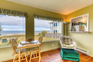 A room with a view of the beach, a dining table with chairs, a cushioned chair, and a small ottoman. - Dog-friendly oceanfront home on a bluff with spectacular views (Bandon)
