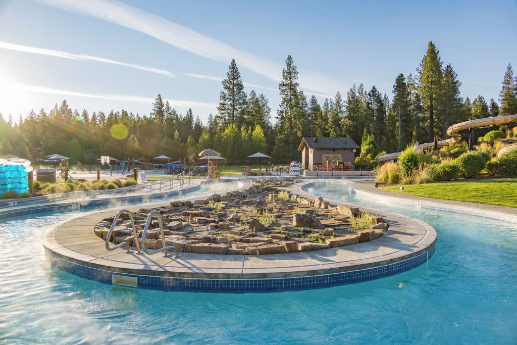 A circular hot tub surrounded by a pool, with a small building and trees in the background.