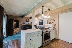 A kitchen with wooden beams, a white countertop, an oven, a microwave, and a hanging light fixture. - Wood-beam cabin with amazing location, pools, hot tub & SHARC passes (Sunriver)