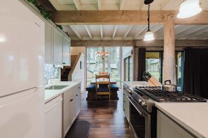 A kitchen with wooden beams, a stove, and a dining area with a table and chairs. - Wood-beam cabin with amazing location, pools, hot tub & SHARC passes (Sunriver)
