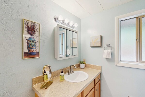 Un bagno con lavandino, mobile contenitore, specchio illuminato e decorazioni a parete.
