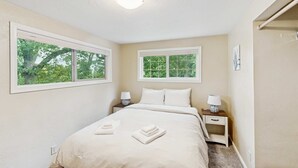 Un dormitorio con una cama, dos mesitas de noche con lámparas, una ventana y una puerta.