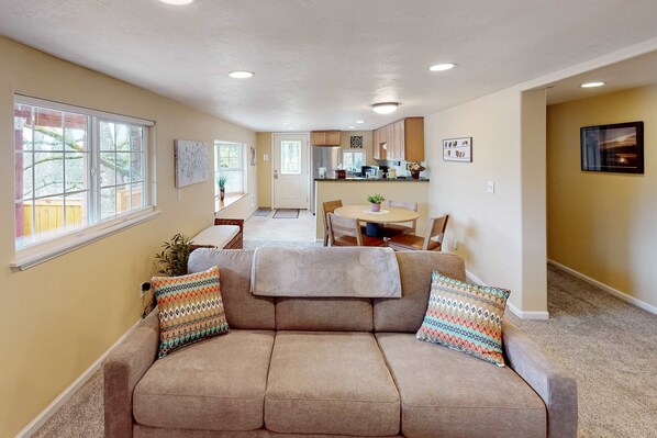 A living room with a sofa, a dining table, and a kitchen in the background.