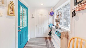 A hallway with a blue door, a white door, a patterned rug, a wooden chair, and a window with a view.