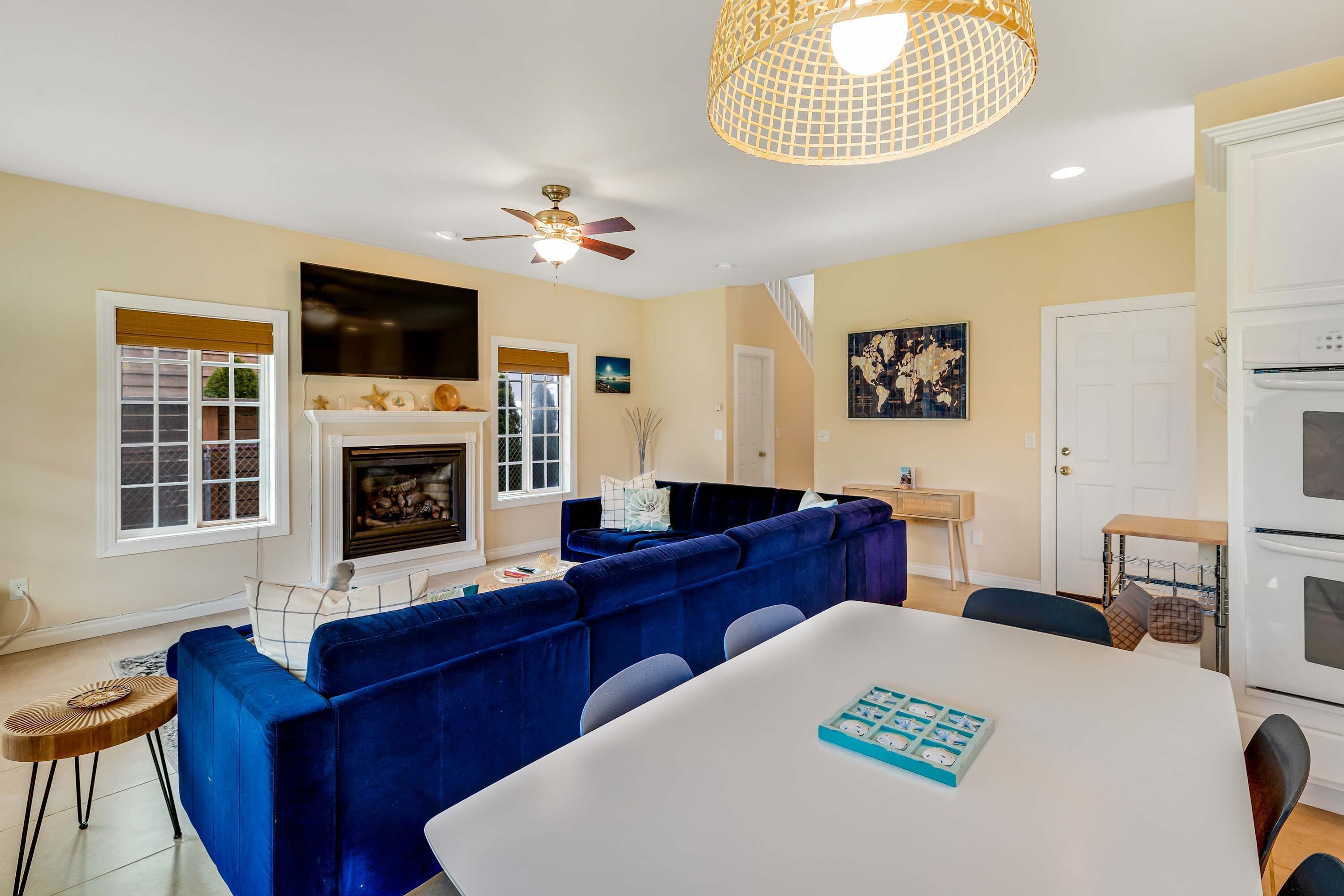 A living room with a fireplace, blue sofas, a dining table, and a ceiling fan.