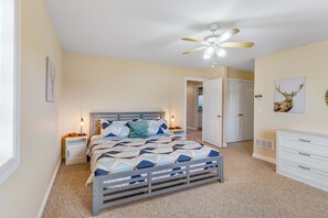 Ein Schlafzimmer mit einem Bett, Nachttischen, einem Deckenventilator, einem Schminktisch und einer Tür zu einem anderen Raum.