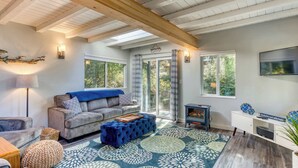 A cozy living room with a sofa, ottoman, and a television. - Stunning new home with furnished deck & easy beach access (Florence)