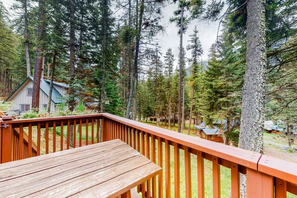 A wooden deck with a view of a forested area and cabins.