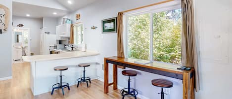 Cocina moderna con una isla central, taburetes de bar y un ventanal con vistas a zonas verdes.