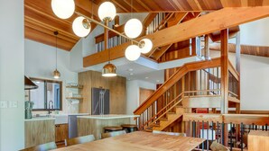 A spacious kitchen with a central island, wooden staircase, and a dining area with a large table. - Dog-friendly home with grill, deck, firepit, balcony, & mountain view (Black Butte Ranch)