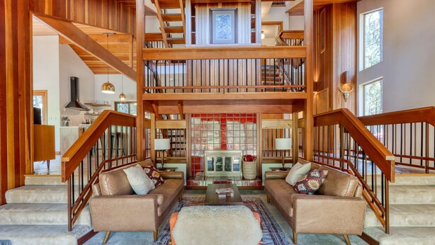 A spacious multi-level living area with a fireplace, wooden staircase, and a cozy seating arrangement. - Dog-friendly home with grill, deck, firepit, balcony, & mountain view (Black Butte Ranch)