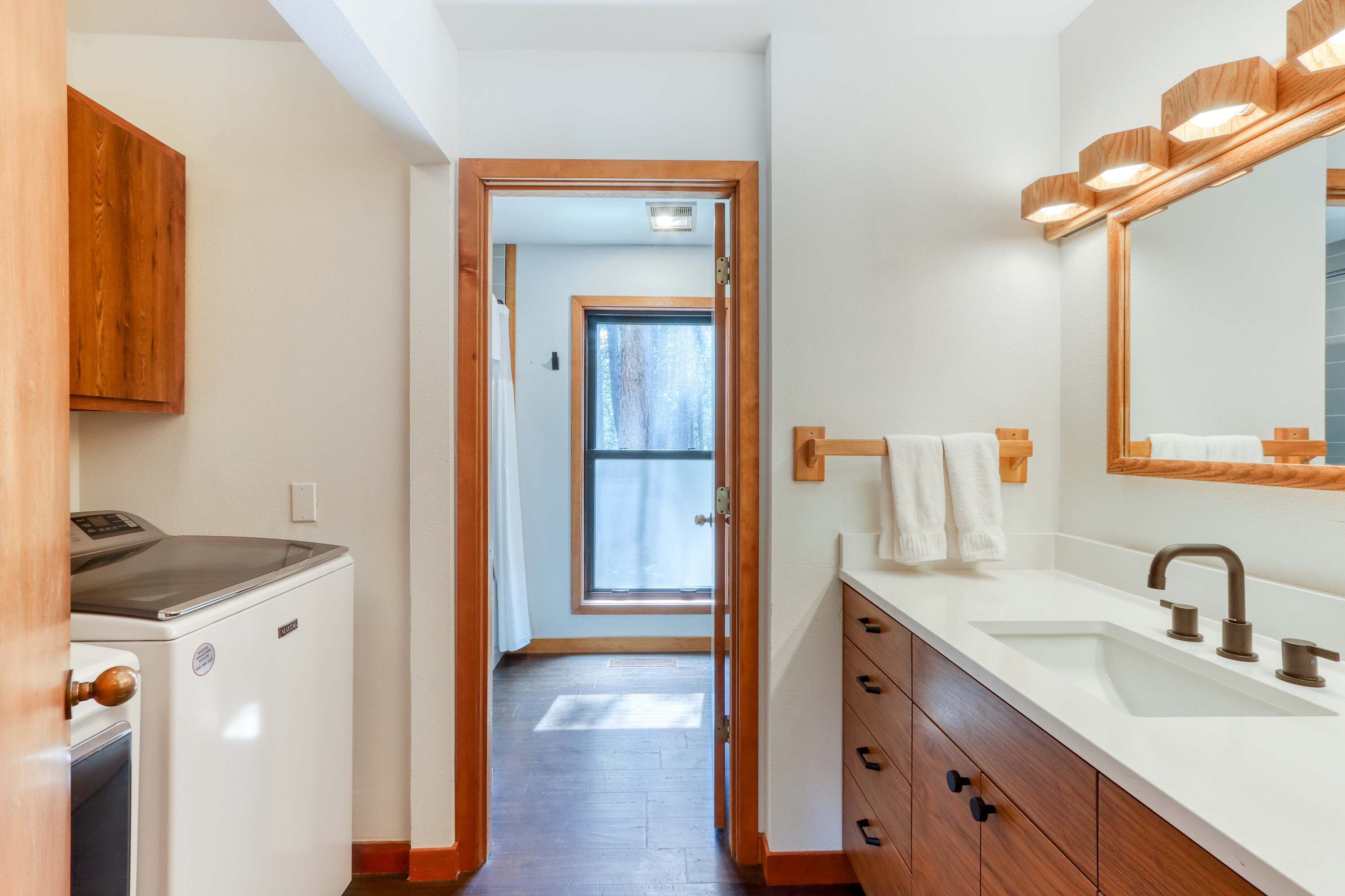 A narrow hallway leading to a bathroom with a sink, mirror, and wooden cabinets.