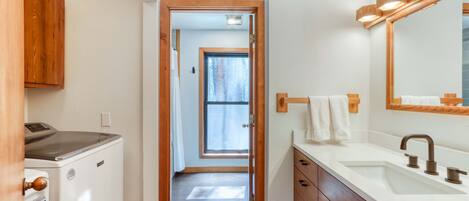 A narrow hallway leading to a bathroom with a sink, mirror, and wooden cabinets.
