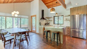 A spacious kitchen with a large island, wooden ceiling beams, and a view of the outdoors. - Dog-friendly home with grill, deck, firepit, balcony, & mountain view (Black Butte Ranch)