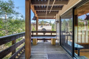 A wooden deck with a bench, a glass door, and a view of buildings and trees. - Spacious, historic lodge with game room, pool, & fireplace - close to Skibowl (Government Camp)